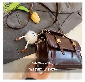 Gros plan d'un sac bandoulière rétro en cuir verni marron avec boucle dorée et pompon blanc