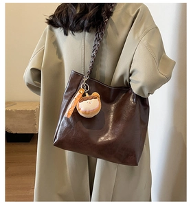 Detail of dark brown glossy tote bag with woven shoulder strap and cute plush charm