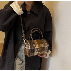 Detail of checkered woolen Boston bag with leather handles on a model in a black coat