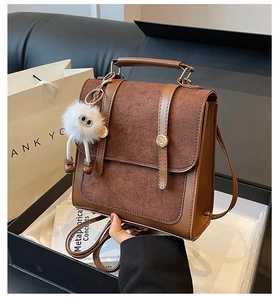 Detailed view of brown suede and leather patchwork backpack with gold buckles and pompom
