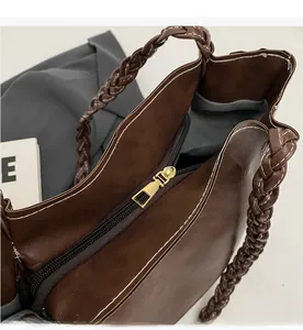 Detail of smooth gold zipper and woven handle on dark brown leather tote bag