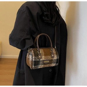 Detail of vintage plaid wool handbag with leather handles worn over a black coat