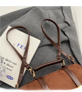 Detail of a brown suede retro handbag with gold hardware styled on a grey blazer suit