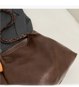 Detail of deep brown tote bag featuring white contrast stitching and woven leather handle