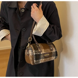 Detail of checkered tweed cylinder bag featuring leather handles and golden metal hardware