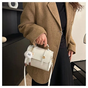Détail d'un sac bandoulière blanc crème brillant avec boucle dorée et pendentif peluche