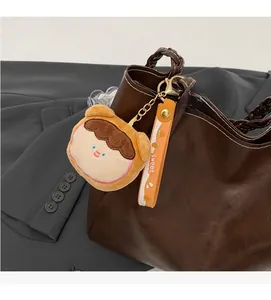 Close-up of a cute plush doll keychain and orange strap on a brown tote bag