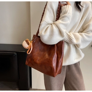 Detail of vintage brown tote bag featuring braided straps and a small doll charm