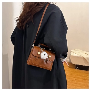 Sac bandoulière en cuir marron avec boucle en métal et peluche porté par un mannequin