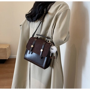 Détail d'un sac à dos vintage marron foncé avec rabat en daim et breloque en peluche blanche
