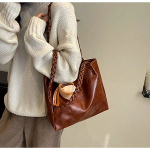 Brown leather tote bag featuring a thick braided shoulder strap and plush charm