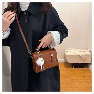 Détail du sac bandoulière en cuir PU marron avec boucle dorée et breloque peluche blanche