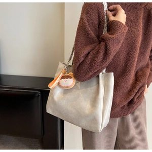 Detail of cream tote bag with woven handles and a cute plush keychain charm for daily commute