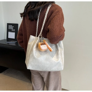 Minimalist white tote bag with woven handles and plush charm shown on shoulder