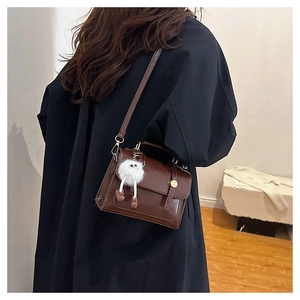 Détail d'un sac bandoulière en similicuir marron avec boucle dorée et pompon en peluche