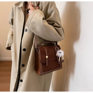Détail d'un sac vintage marron avec breloque monstre en peluche sur un trench-coat