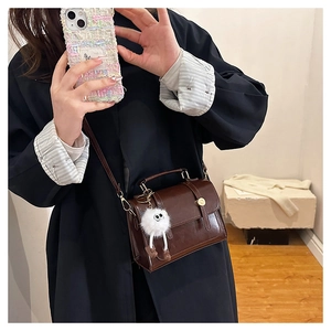 Détail du sac bandoulière vintage en cuir PU marron avec un charme de monstre en peluche blanc