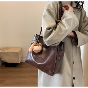 Detail of dark brown oil wax leather tote with braided handle and plush charm accessory