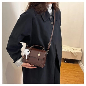 Détail du sac bandoulière marron foncé en cuir avec un pendentif oiseau en peluche blanc