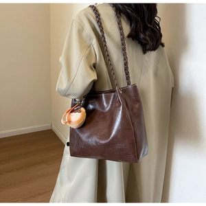Brown leather tote bag detail with braided straps and a cute cartoon charm on a shoulder