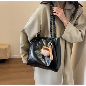 Close-up of black glossy tote bag featuring woven handles and a cute plush charm