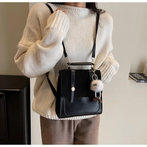 Détail du sac bandoulière en cuir noir avec textures mixtes et breloque monstre