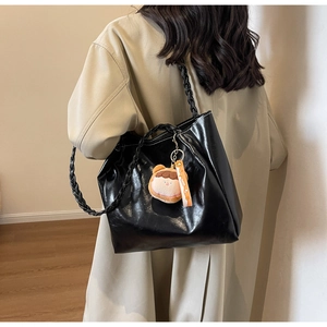 Detail of black glossy tote bag with woven shoulder strap and cute plush charm pendant