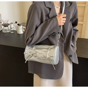 Detail of silver pillow bag with bow accents and pleated texture on a crossbody strap