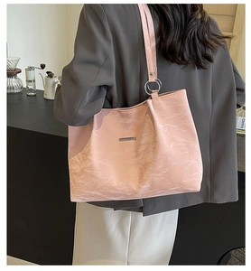 Detail of pink pleated tote bag with metal logo on model in a modern cafe setting