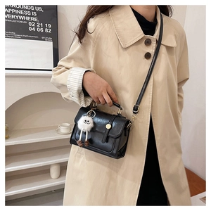 Détail du sac bandoulière noir en cuir PU avec boucle dorée et charm peluche sur trench-coat
