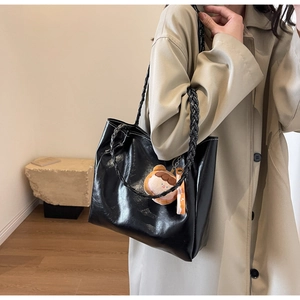 Detail of black glossy tote bag with woven straps and cute bear charm pendant