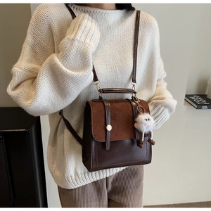 Détail du sac à dos vintage bicolore avec rabat en daim, ferrures dorées et breloque peluche