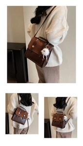 Detail of vintage brown satchel with suede flap, metal buckles, and plush monster charm