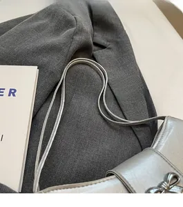Detail einer silbernen Metallic-Tasche mit polierter Schleifenschnalle und schmalen Trägern