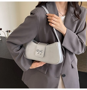 Nahaufnahme einer silbernen Schultertasche mit Metallschleife auf grauem Blazer