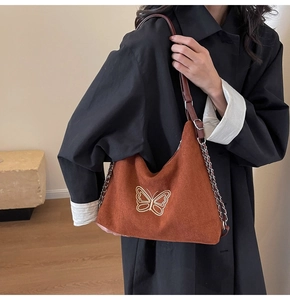 Detail of brown suede shoulder bag featuring white butterfly embroidery and chain strap