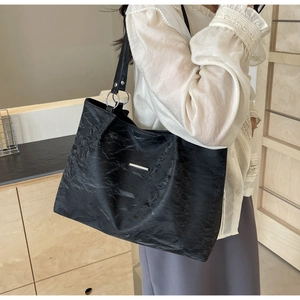 Minimalist black pleated tote bag with silver metal accents shown on shoulder