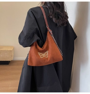 Detail of caramel suede shoulder bag featuring gold butterfly embroidery and chain strap