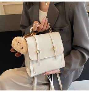 Detail der cremeweißen Ledertasche mit Goldschnallen und braunem Plüsch-Anhänger