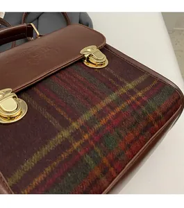 Detail of red and green plaid fabric with brown leather flap and metallic dual buckles