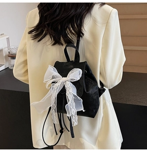 Detail of velvet backpack with large white lace bow on back of female model in white blazer