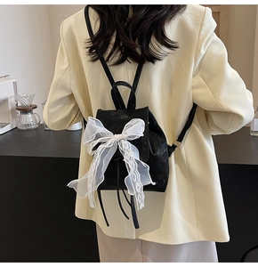 Detail of black backpack with a large white lace bow shown on a model's back