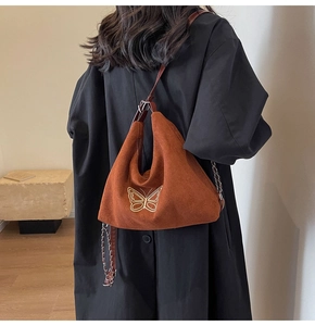 Detail showing butterfly embroidery and metal chain on a brown suede shoulder bag