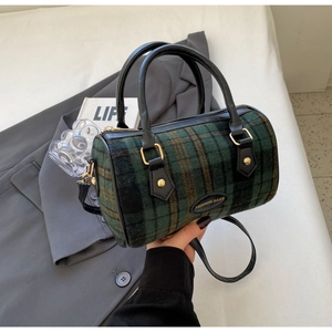 Close-up of retro green plaid cylinder bag with leather handles and gold hardware details