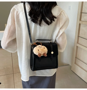 Detail view of black faux leather crossbody bag with a plush bear charm on white shirt