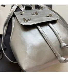 Silver matte backpack with gold butterfly buckles on a minimalist flap cover