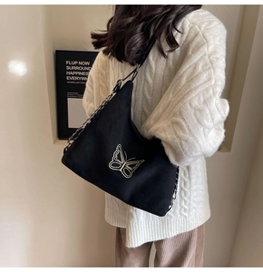 Detail of a black tote bag featuring gold butterfly embroidery and a stylish chain strap