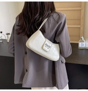 Detailansicht einer cremeweißen Baguette-Tasche mit silberner Schleife an einem Model