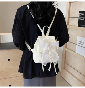 Detail of cream white mini backpack featuring a large lace bow and slim leather straps