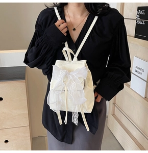 Detail of cream white backpack featuring a large lace bow and delicate ribbon accents